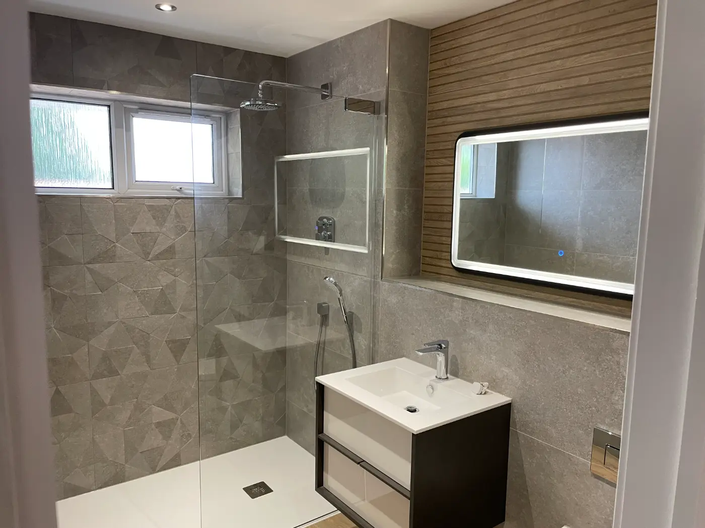 Renovated bathroom with a walk-in shower, geometric grey tiles, timber-effect feature wall and LED mirror