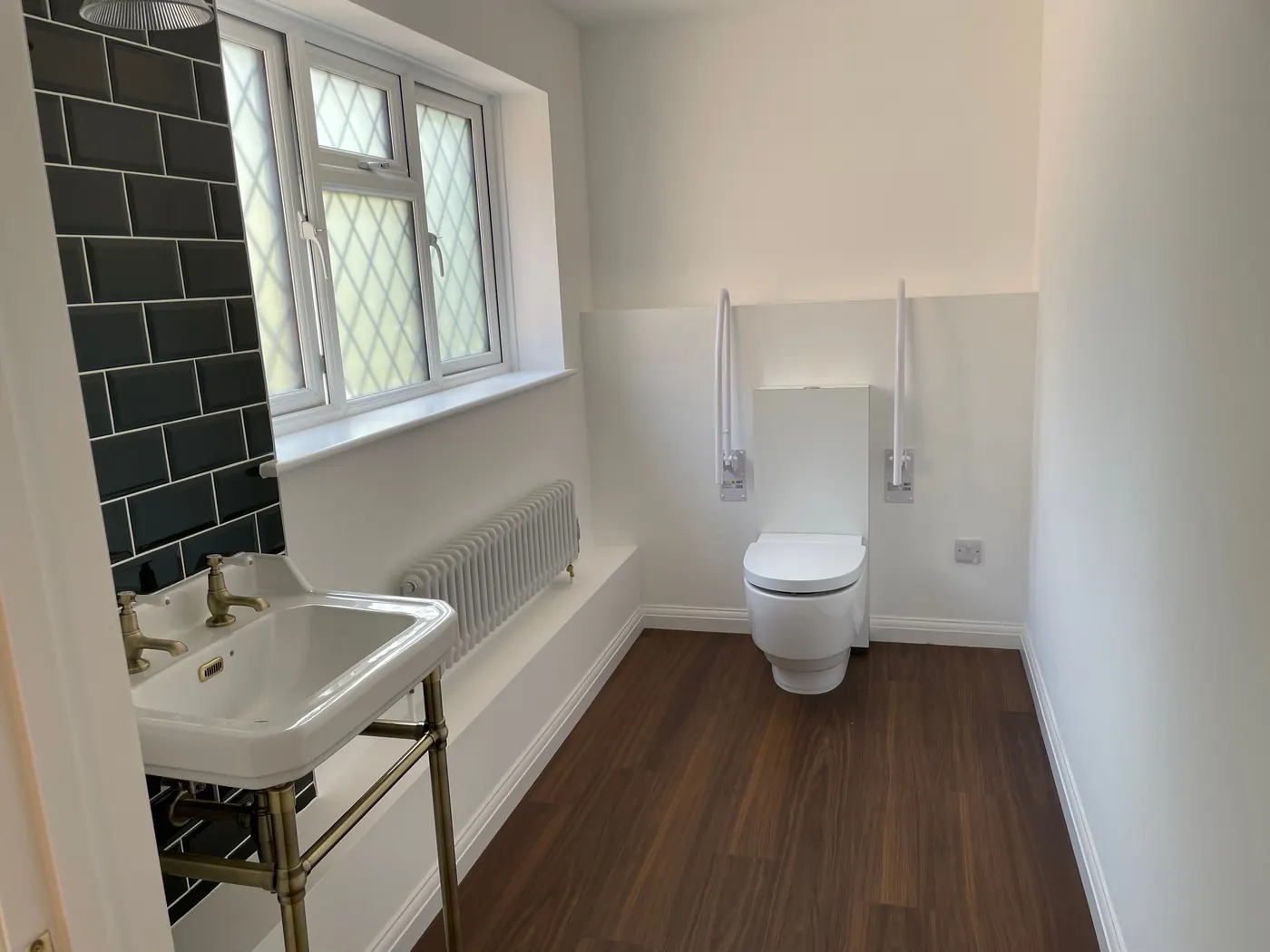 An accessible WC with fold down grab rails, a washstand basin and a dark tiled wall