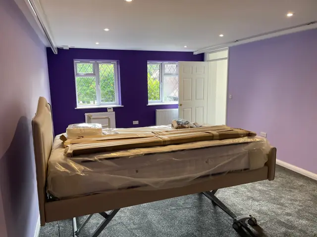 A bedroom with a ceiling hoist track, an adjustable bed and purple walls