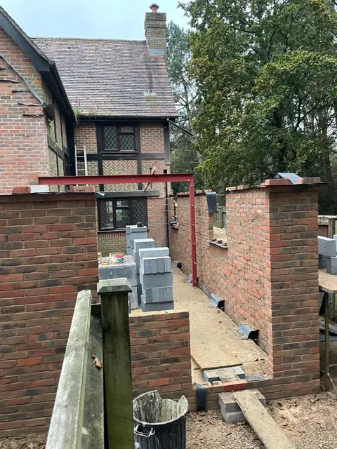 New brick walls of the extension rising beside the house, with a red steel frame spanning between them