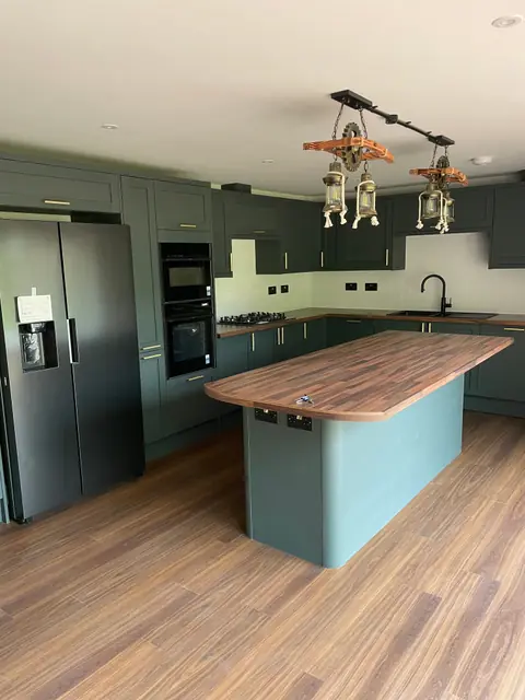 The kitchen island, with a wood worktop, green units and pendant lights
