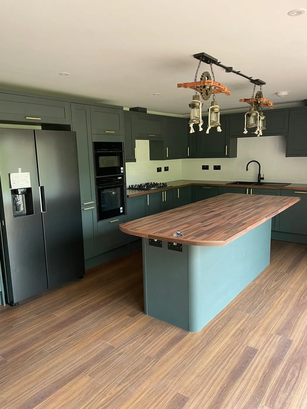The kitchen island, with a wood worktop, green units and pendant lights