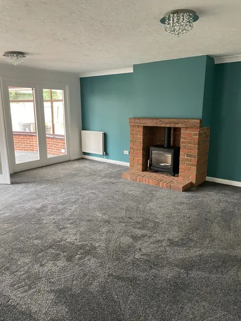 A living room with a teal chimney breast, a brick fireplace with a log burner, and French doors