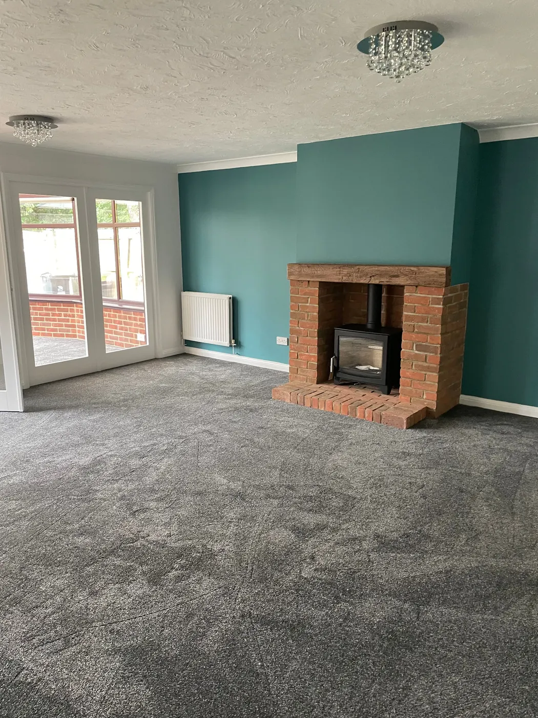 A living room with a teal chimney breast, a brick fireplace with a log burner, and French doors