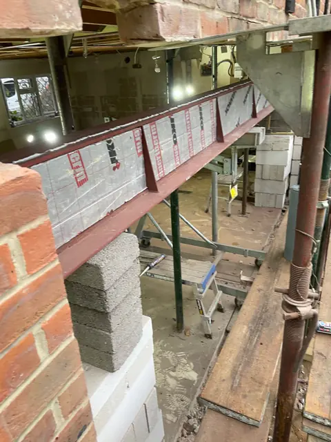 A long steel beam installed across the rear wall, with temporary props and blockwork