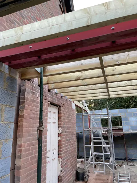 A red steel beam and post carrying new timber floor joists inside the extension
