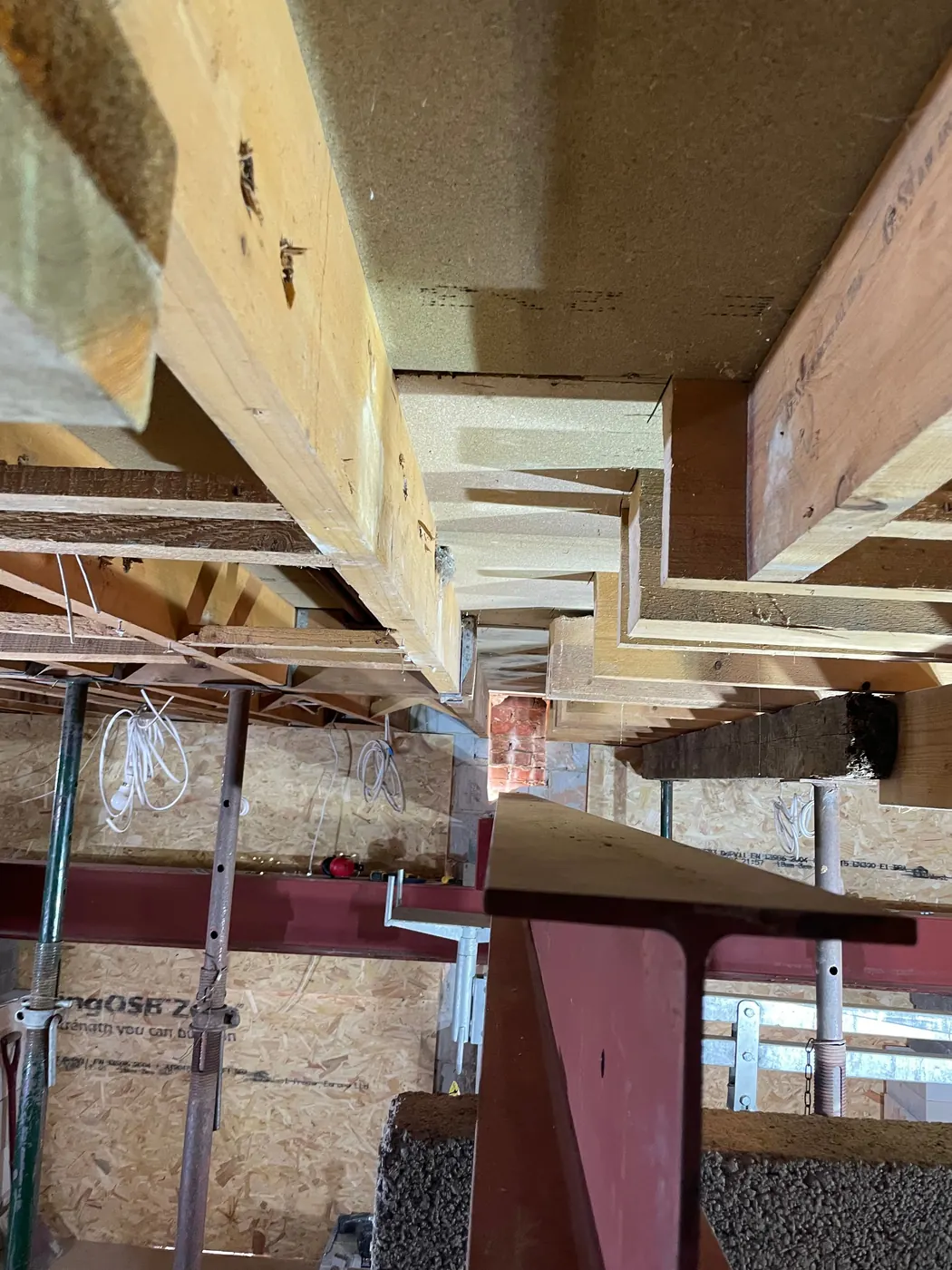 Looking up at a steel beam carrying the floor joists above, with temporary props below