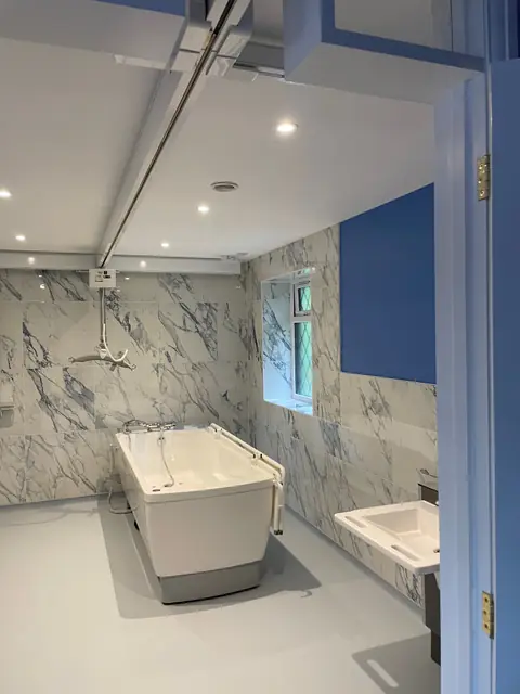 The finished wet room, with a ceiling hoist track above a height adjustable bath and marble effect wall panels