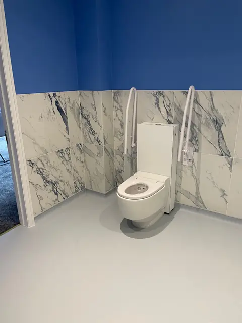 A wet room toilet with fold down grab rails and marble effect wall panels