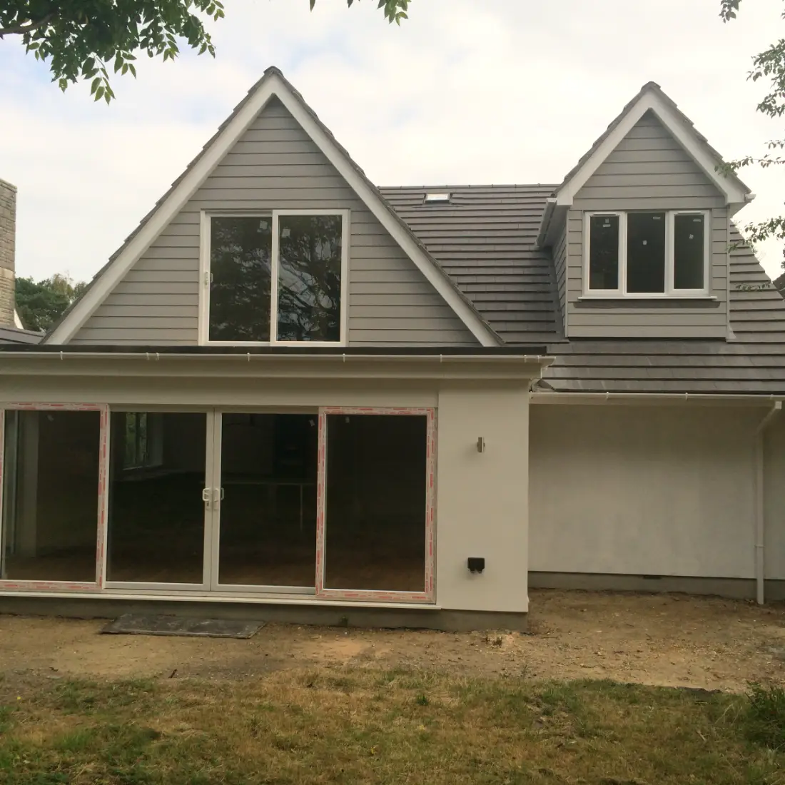 Rear elevation of a two-storey extension finished in grey cladding with white render below and new sliding doors