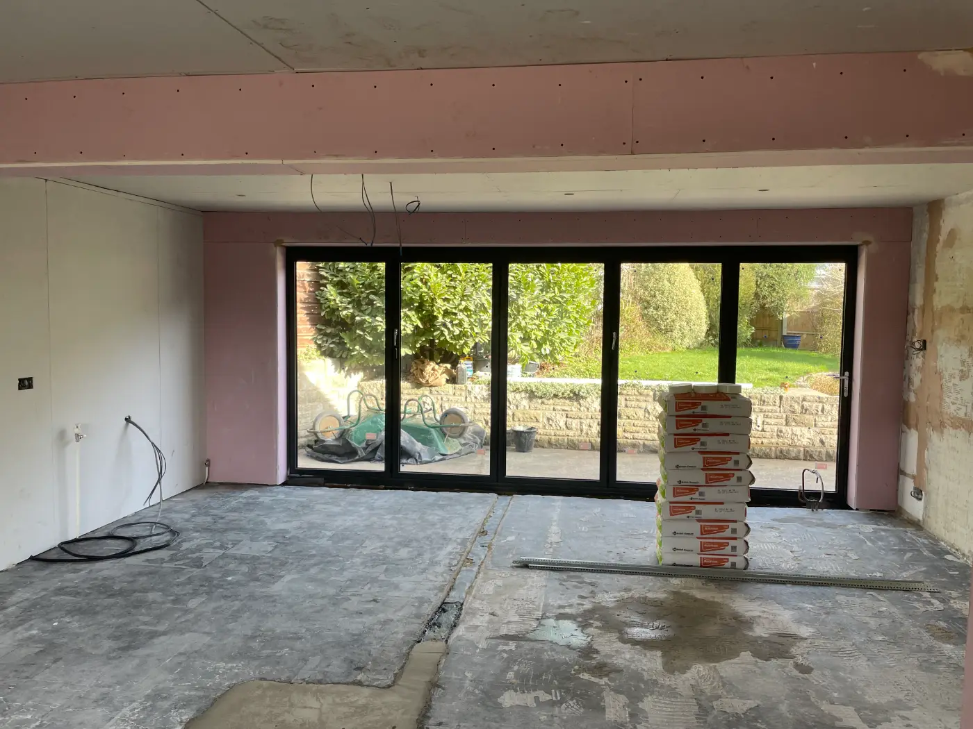 Before: Kitchen extension before fit-out, with bare plasterboard, exposed cables and new bi-fold doors