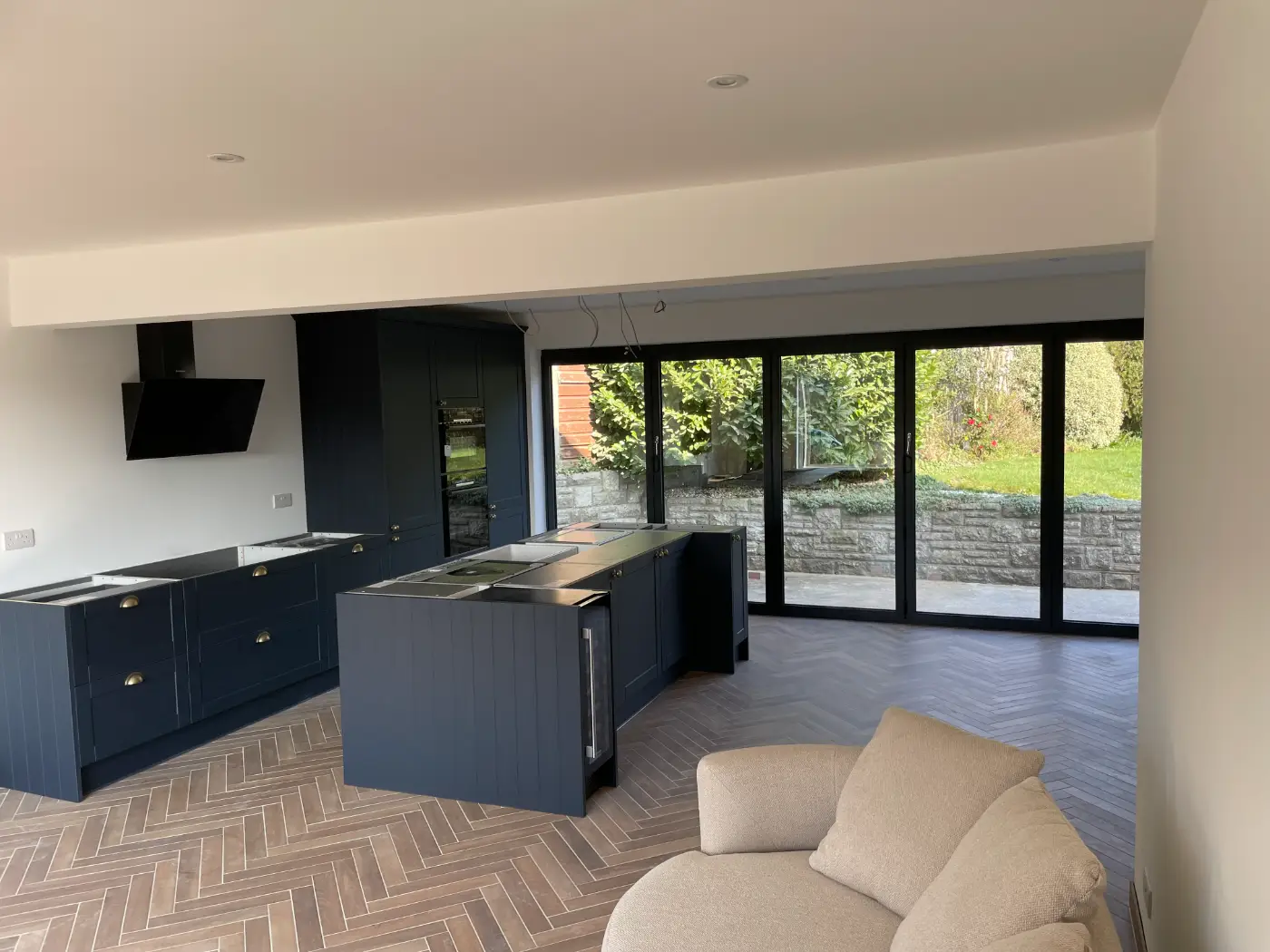 Newly fitted navy shaker kitchen with an island, herringbone floor and bi-fold doors onto the garden