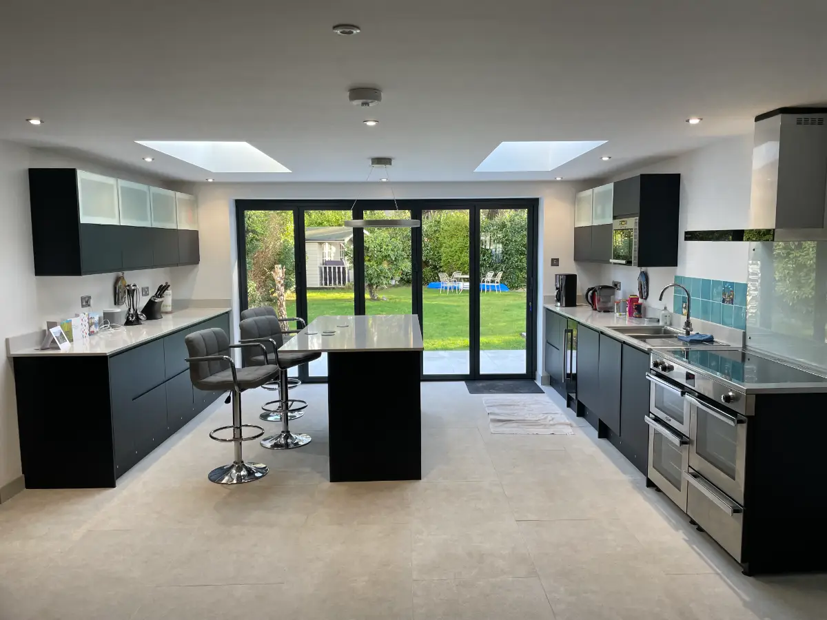 Open-plan kitchen inside a completed rear extension, with an island, two roof lanterns and bi-fold doors onto the garden