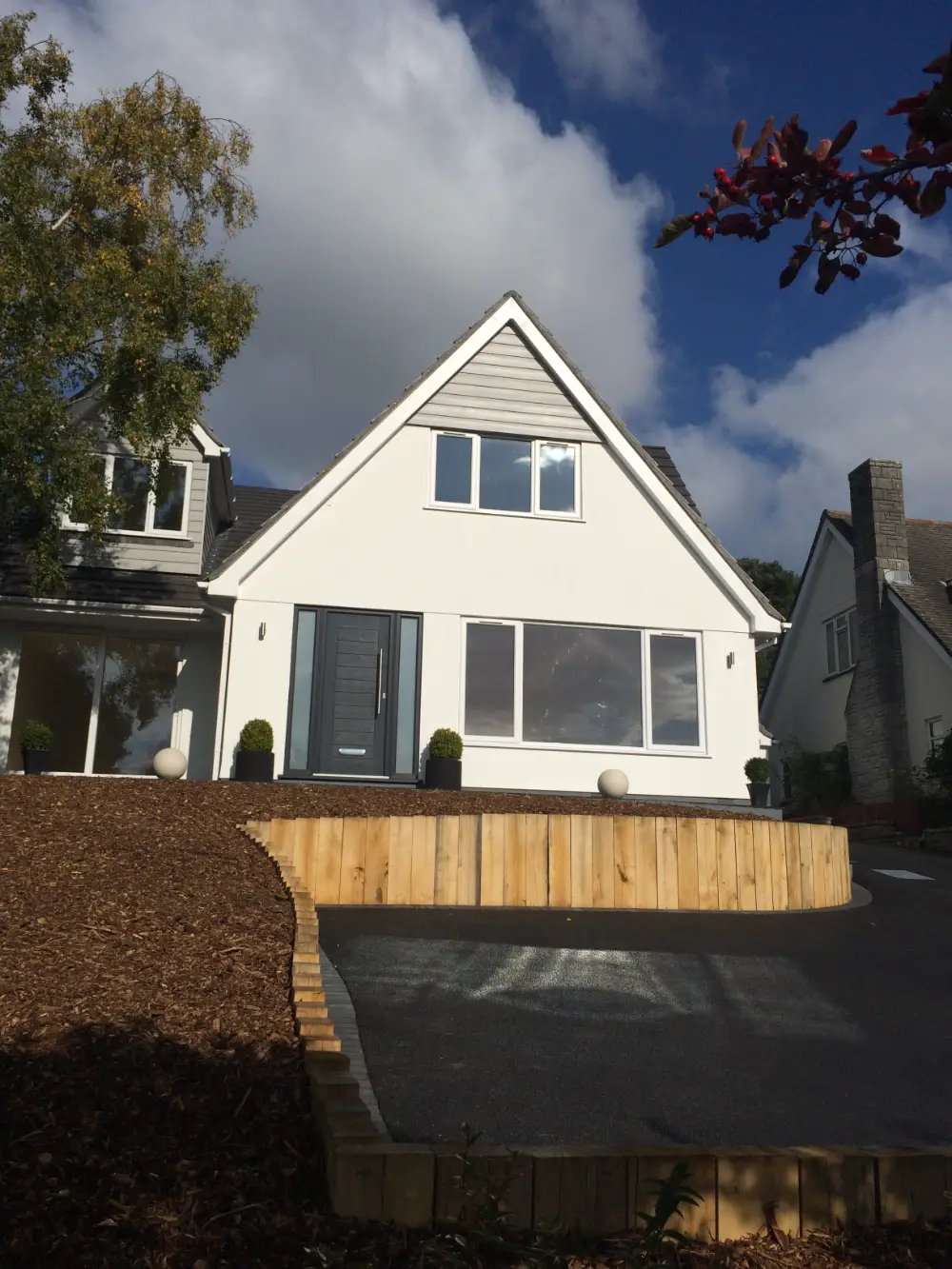 Finished rendered chalet front with grey cladding, oak sleeper retaining wall and new driveway