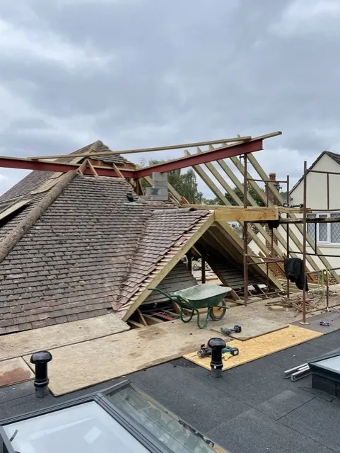 Red steel beams spanning the opened up original tiled roof, with new timber rafters going up for a gable end